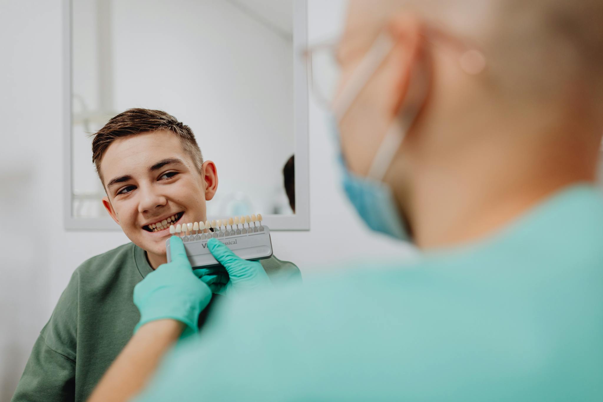 A young boy smiling in a dental clinic while comparing tooth shades.